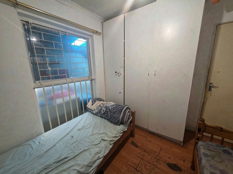 A bedroom featuring built-in cupboards, laminate flooring, and security bars on the window, requiring cosmetic updates to improve its overall condition.