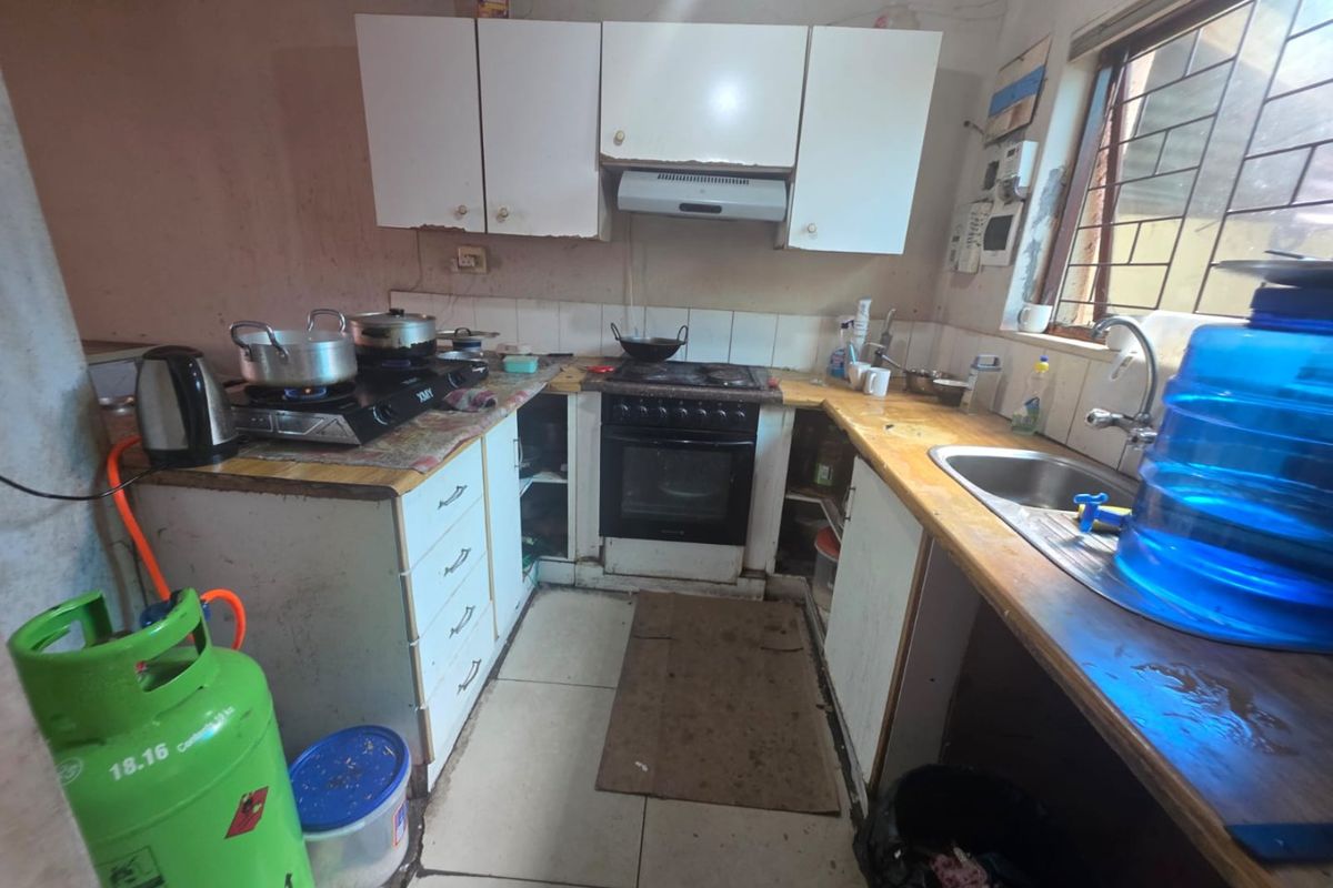 A compact kitchen featuring built-in cabinetry, a stainless steel sink, and a freestanding oven, requiring cosmetic updates to improve its overall condition.