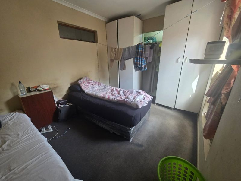 A bedroom featuring built-in cupboards and carpeted flooring, currently in need of cosmetic updates and maintenance.