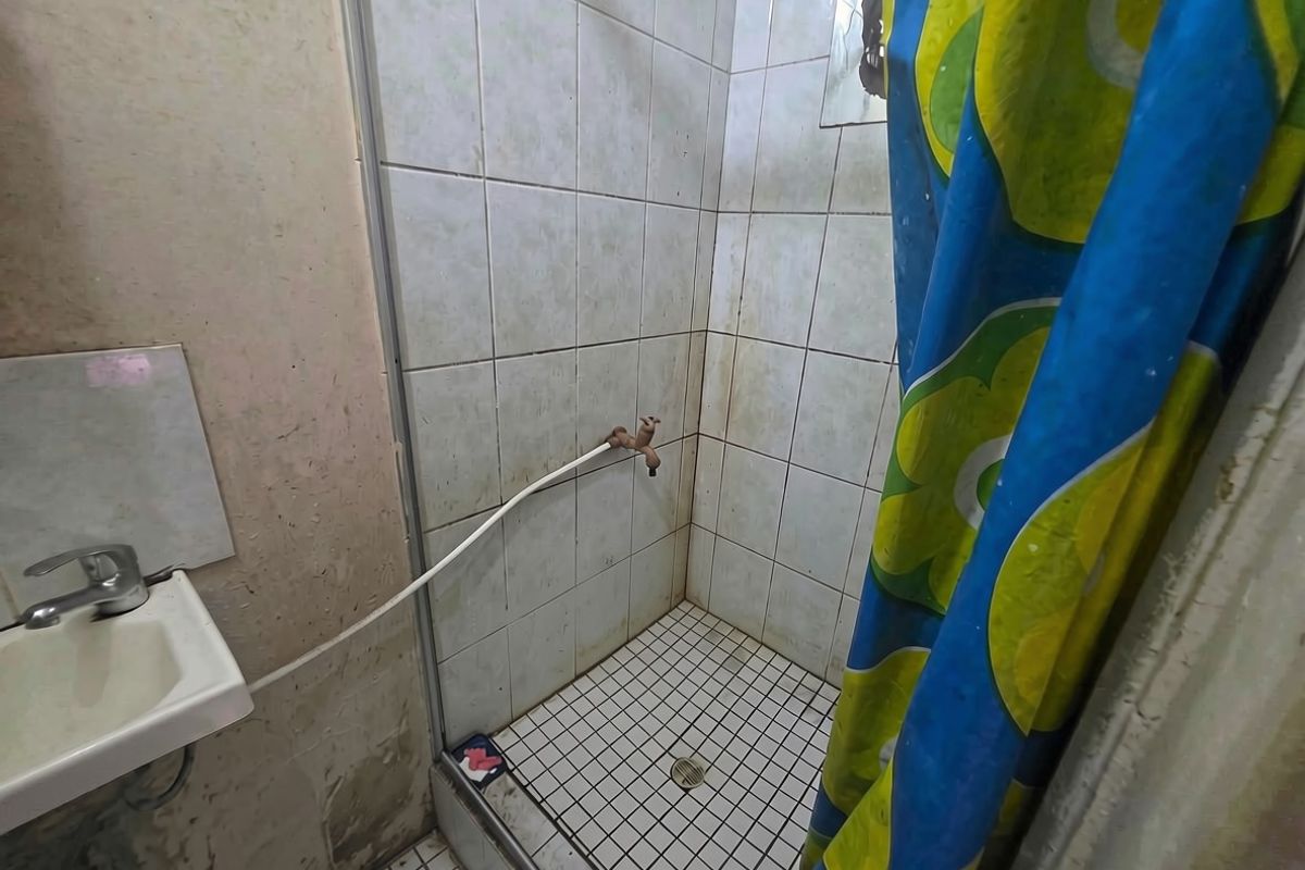 A compact bathroom featuring a tiled shower enclosure and a wall-mounted basin, currently showing significant signs of wear and requiring maintenance or renovation.