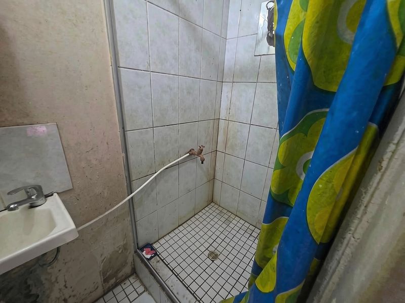A compact bathroom featuring a tiled shower enclosure and a wall-mounted basin, currently showing significant signs of wear and requiring maintenance or renovation.