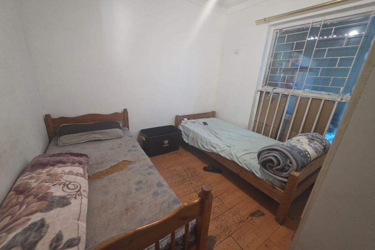 A bedroom featuring security bars on the window and wooden flooring, currently utilized with twin beds.
