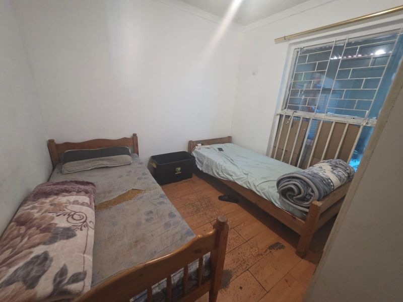 A bedroom featuring security bars on the window and wooden flooring, currently utilized with twin beds.