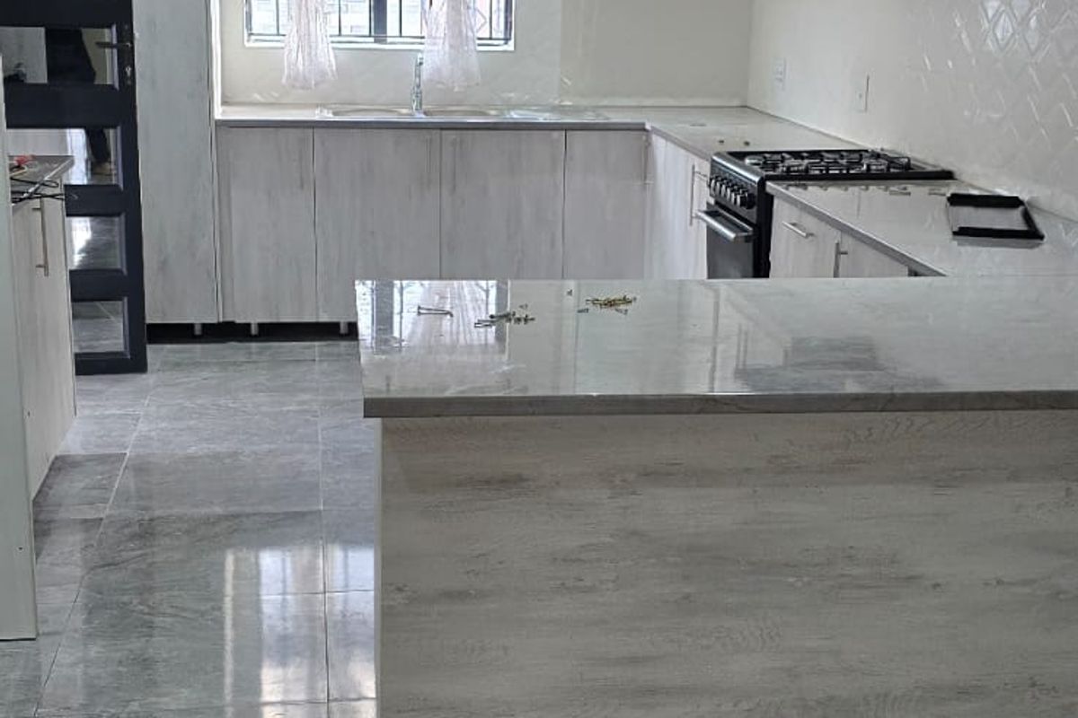 Modern kitchen featuring light wood-grain cabinetry, stone countertops, a central island, and high-gloss tiled flooring with integrated gas stove and extractor fan.