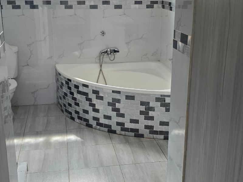 A clean bathroom featuring a corner bathtub, tiled walls with decorative accents, and tiled flooring, providing a functional and well-maintained space.