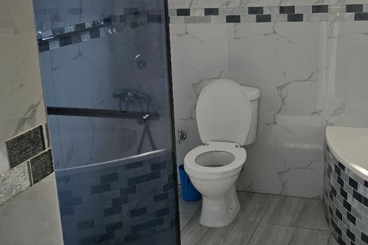 A modern bathroom featuring a glass-enclosed shower, toilet, and contemporary marble-effect wall tiling with decorative mosaic accents.