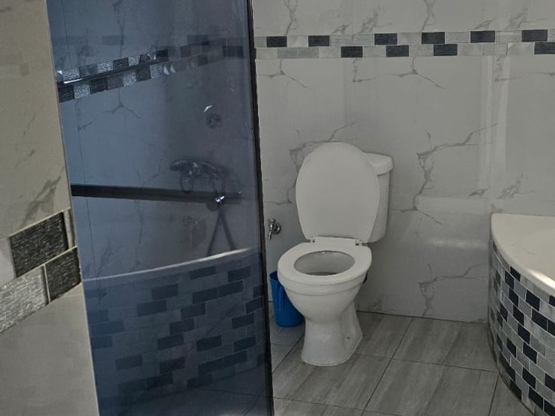 A modern bathroom featuring a glass-enclosed shower, toilet, and contemporary marble-effect wall tiling with decorative mosaic accents.