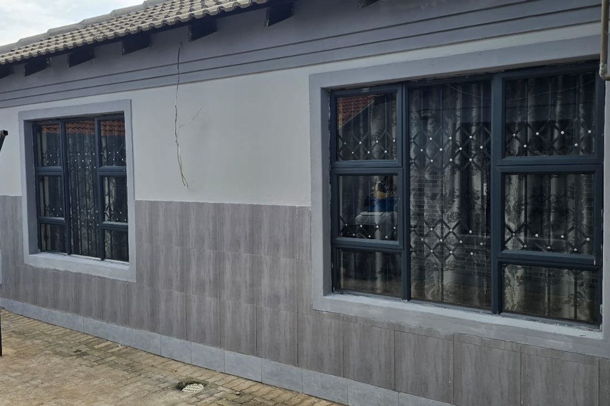 Rear exterior view of the property featuring tiled wall cladding, aluminium window frames with security bars, and a paved outdoor area.