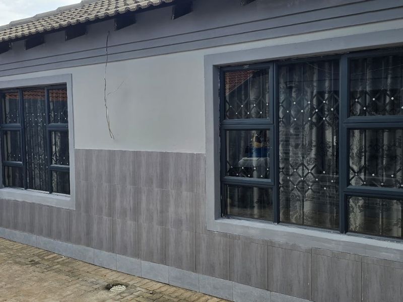 Rear exterior view of the property featuring tiled wall cladding, aluminium window frames with security bars, and a paved outdoor area.