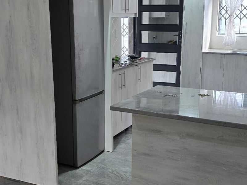 Modern kitchen featuring light wood-grain cabinetry, stone countertops, a central island, and dark grey tiled flooring with recessed lighting.
