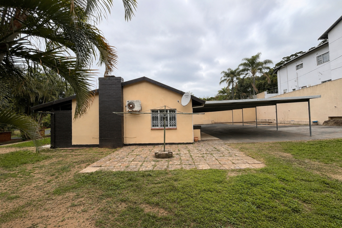 Rear view of the property featuring a paved patio area, a large carport, and an exterior brick chimney.