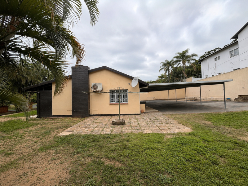 Rear view of the property featuring a paved patio area, a large carport, and an exterior brick chimney.