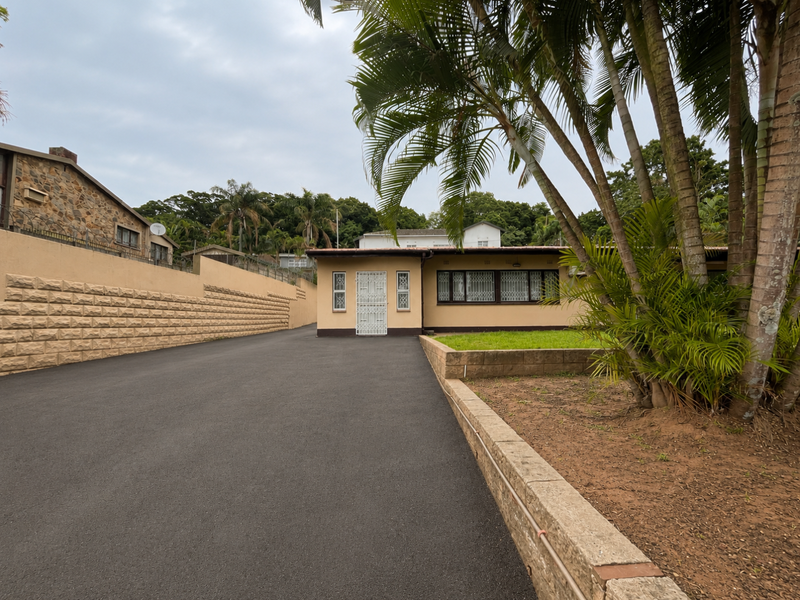 Front view of the property featuring a paved driveway, retaining walls, and a secure entrance with security bars.