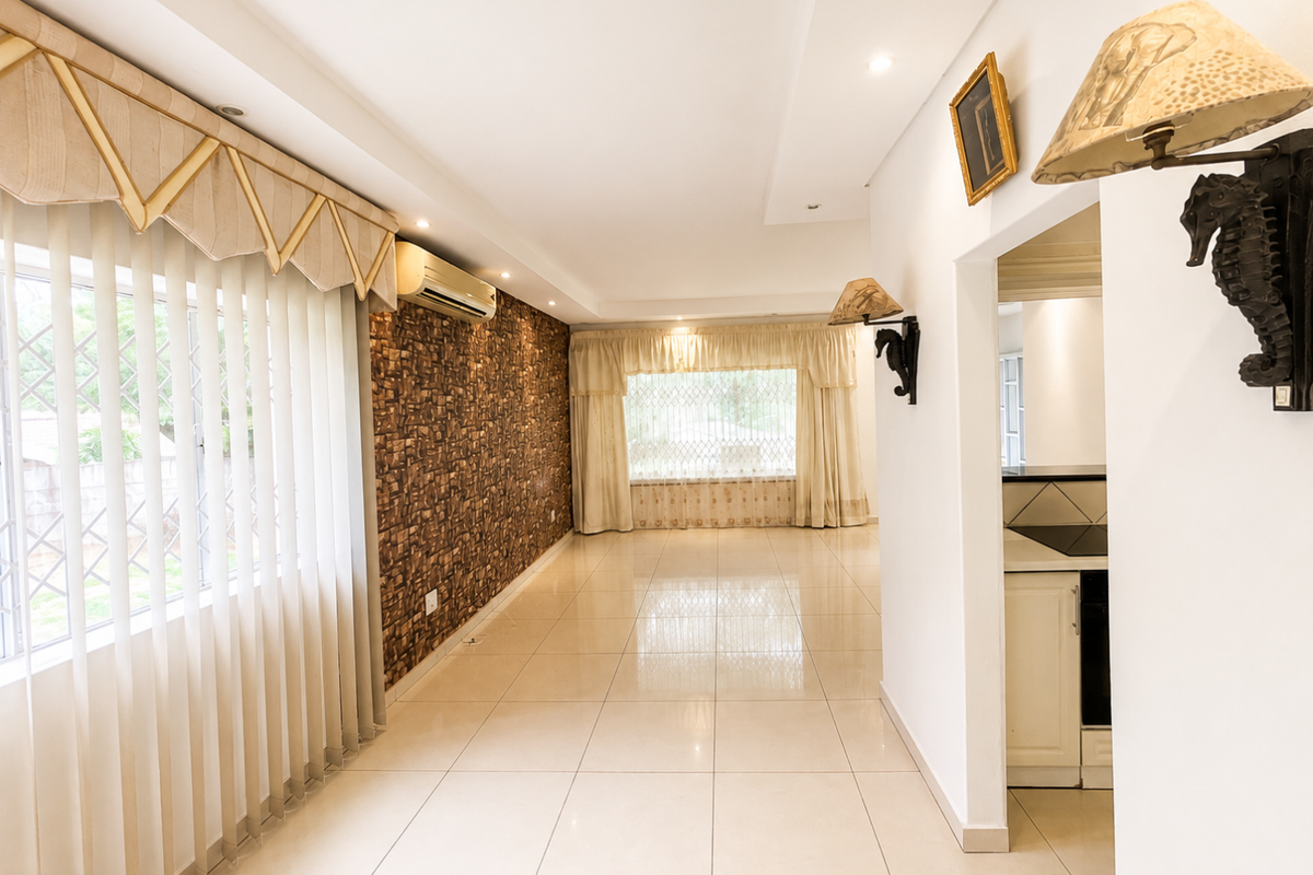Spacious living area featuring polished tiled flooring, a textured feature wall, and a wall-mounted air conditioning unit, with an open flow to the kitchen area.
