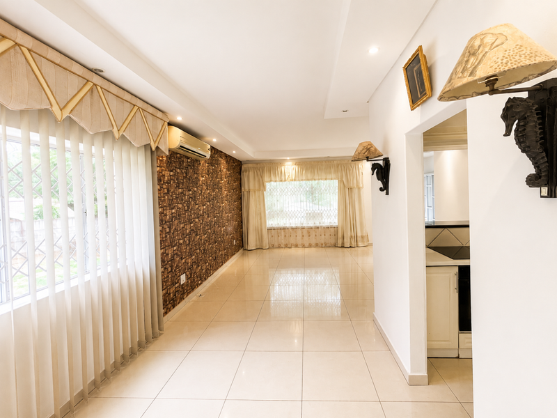 Spacious living area featuring polished tiled flooring, a textured feature wall, and a wall-mounted air conditioning unit, with an open flow to the kitchen area.