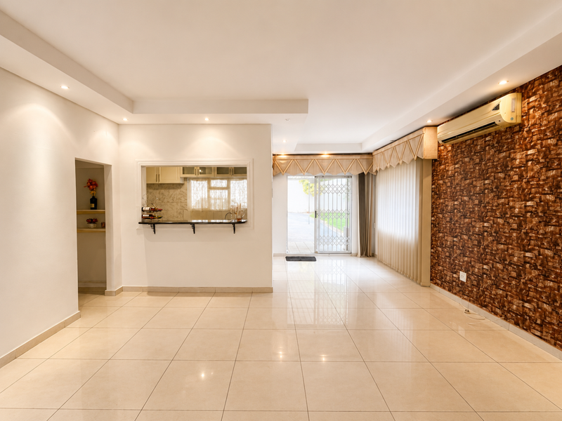 Spacious living area featuring polished tile floors, a stone-cladding feature wall, split-system air conditioning, and a convenient pass-through window connecting to the kitchen.