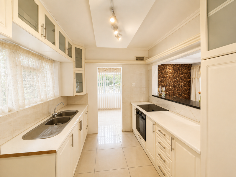 A clean, functional kitchen featuring white cabinetry, tiled flooring, a double sink, and a convenient pass-through window overlooking the adjacent living area.