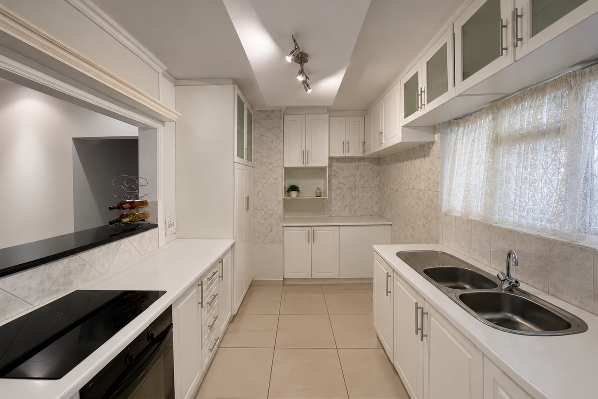 A clean, well-maintained kitchen featuring white cabinetry, tiled flooring, a double sink, and integrated appliances with a convenient pass-through window to the living area.