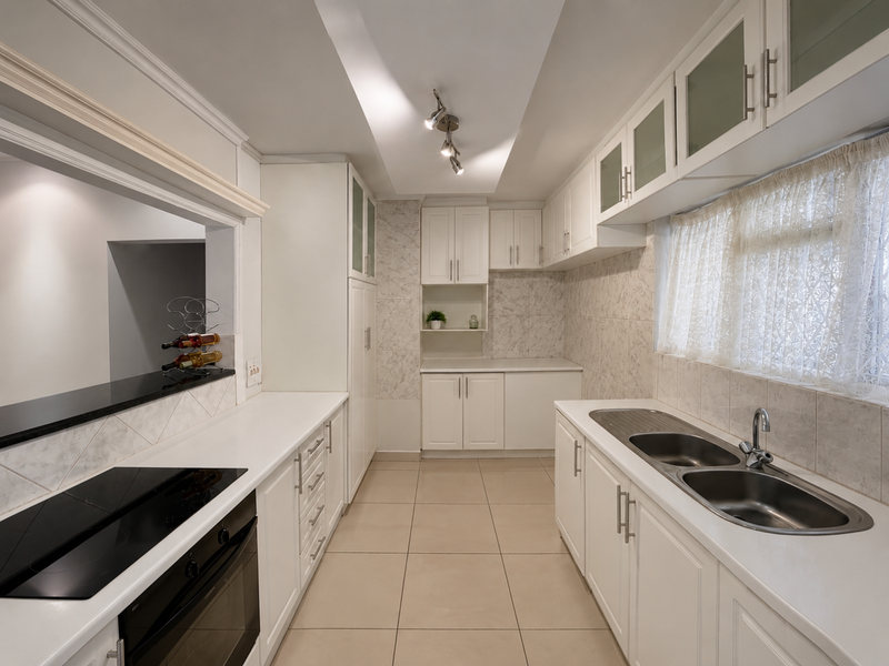 A clean, well-maintained kitchen featuring white cabinetry, tiled flooring, a double sink, and integrated appliances with a convenient pass-through window to the living area.