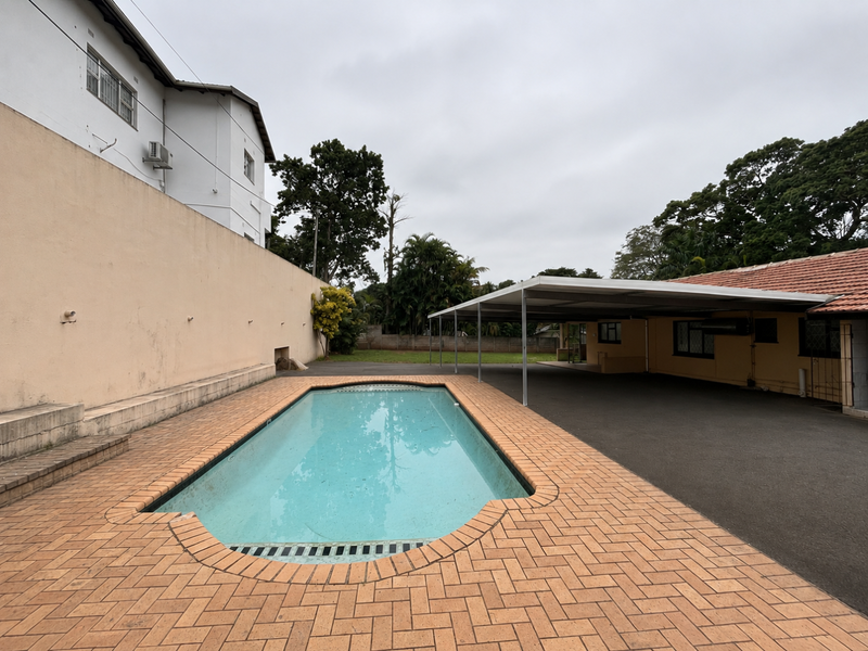Outdoor pool area featuring brick paving, a large swimming pool, and an adjacent covered carport structure.