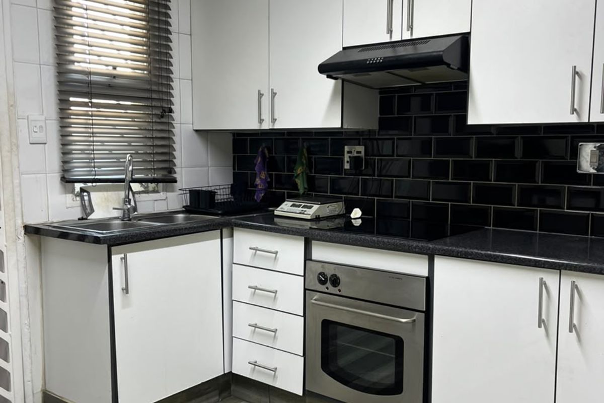 Compact kitchen featuring white cabinetry, black subway tile backsplash, stainless steel oven, electric cooktop, and wood-look laminate flooring.