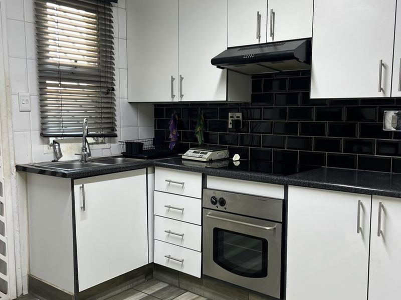 Compact kitchen featuring white cabinetry, black subway tile backsplash, stainless steel oven, electric cooktop, and wood-look laminate flooring.