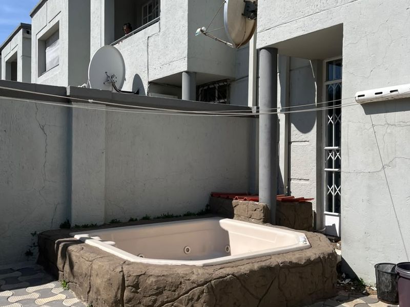 Rear exterior area featuring a built-in jacuzzi, paved patio flooring, and direct access to the home via a security gate.