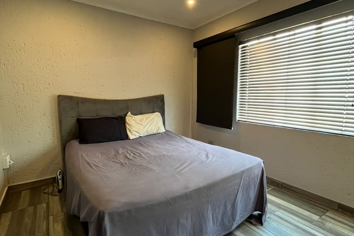 A bedroom featuring modern wood-look tiled flooring, recessed downlighting, and venetian blinds, providing a clean and functional living space.