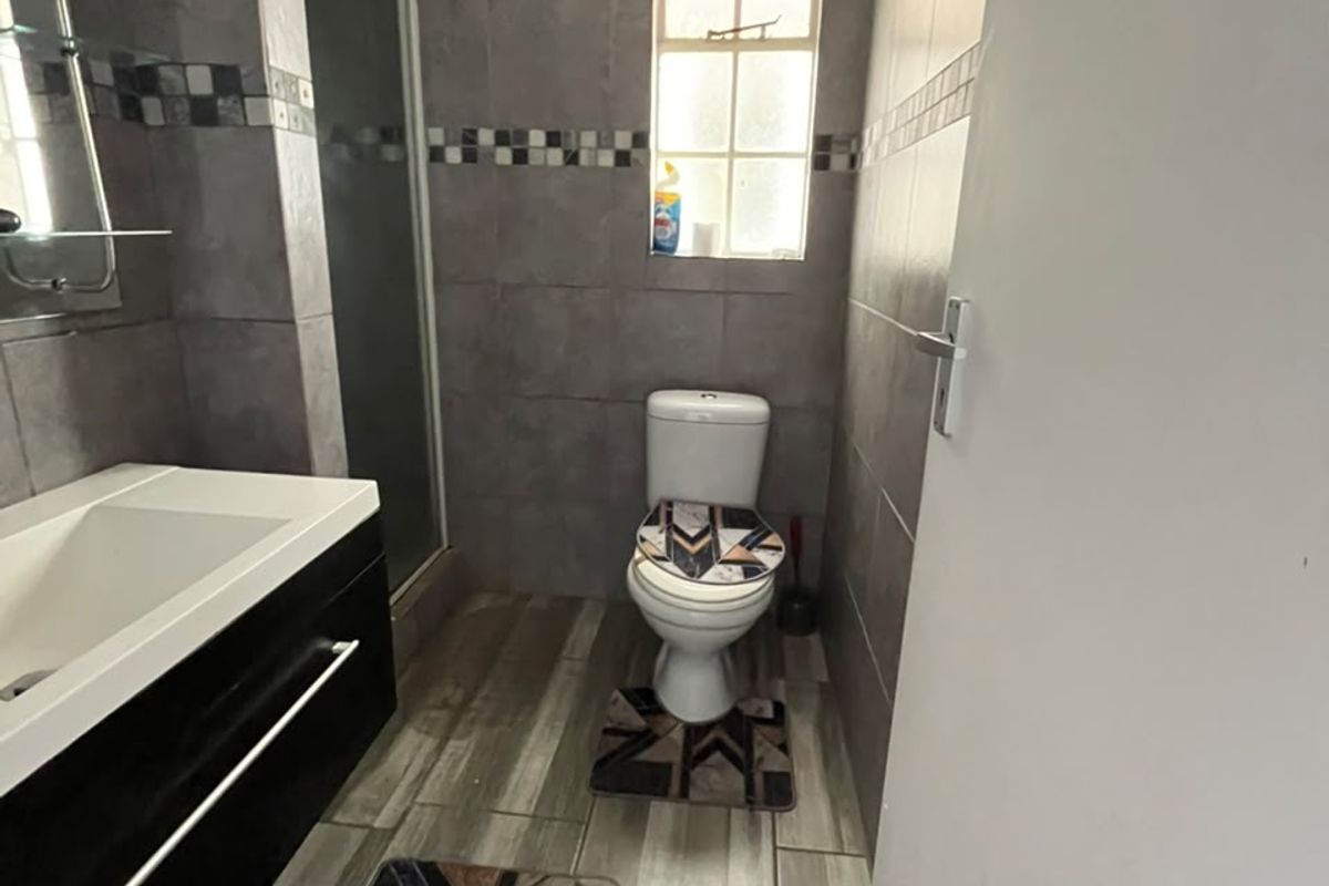 A functional bathroom featuring a modern vanity cabinet, a shower enclosure, and neutral wall and floor tiling.