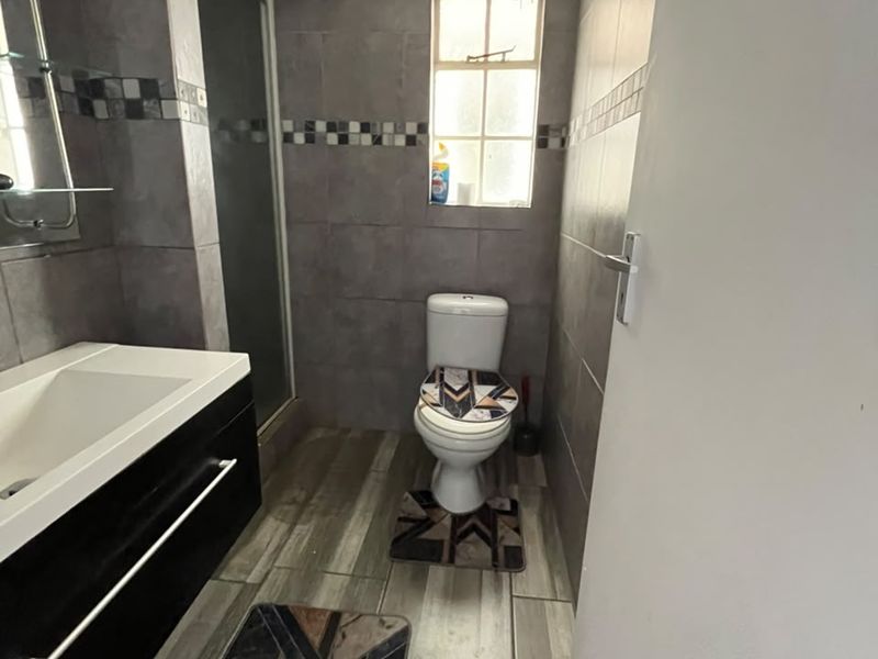 A functional bathroom featuring a modern vanity cabinet, a shower enclosure, and neutral wall and floor tiling.