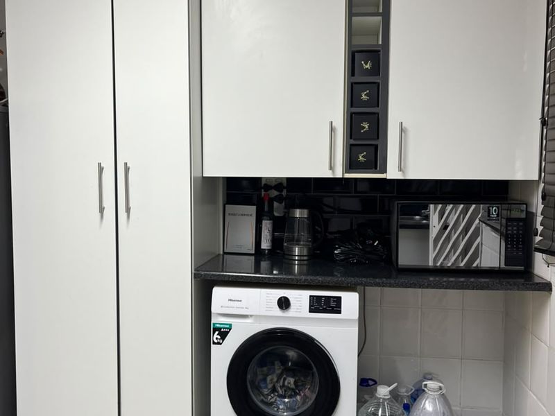 A functional laundry area featuring white built-in cabinetry, dark granite countertops, subway tile backsplash, and wood-look laminate flooring.
