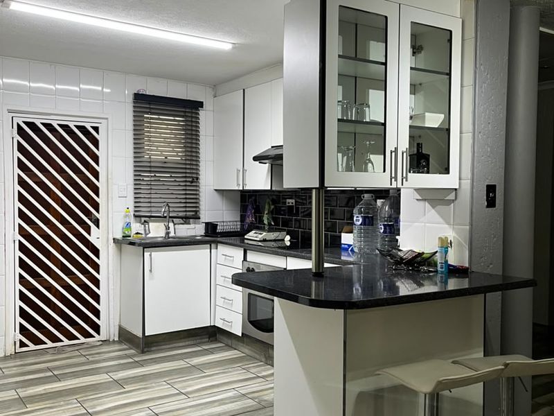 A functional kitchen featuring white cabinetry, black granite countertops, integrated appliances, and wood-look floor tiles with a secure exterior door.
