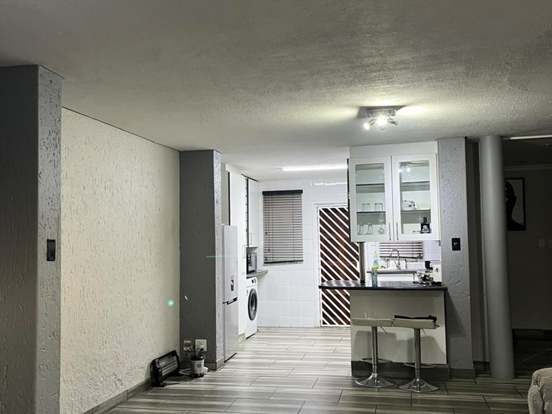 Open plan living area featuring a kitchen with breakfast counter, tiled flooring, and structural columns, providing a functional and connected living space.