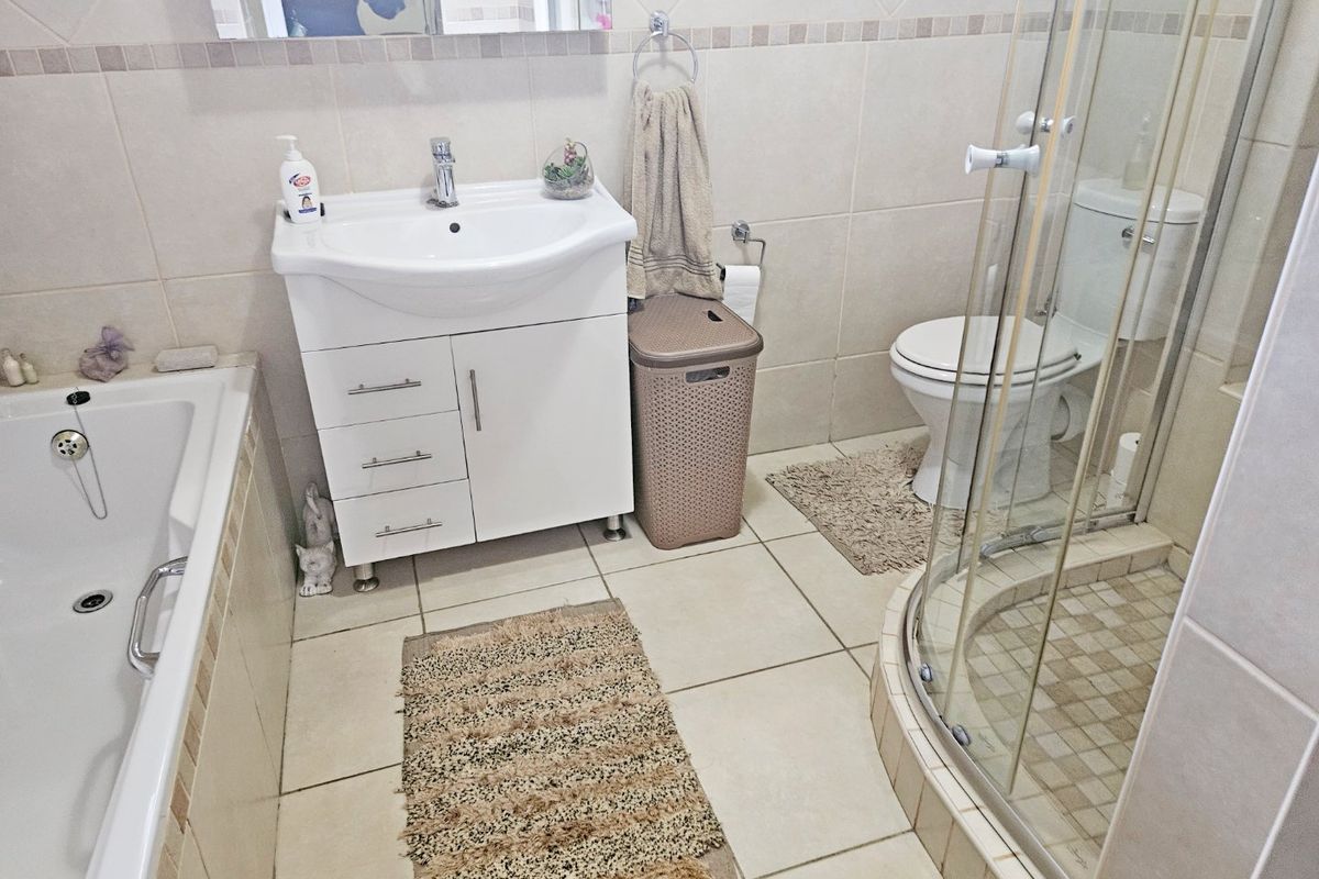 A functional bathroom featuring a vanity unit, bathtub, separate shower enclosure, and toilet with neutral wall and floor tiling.