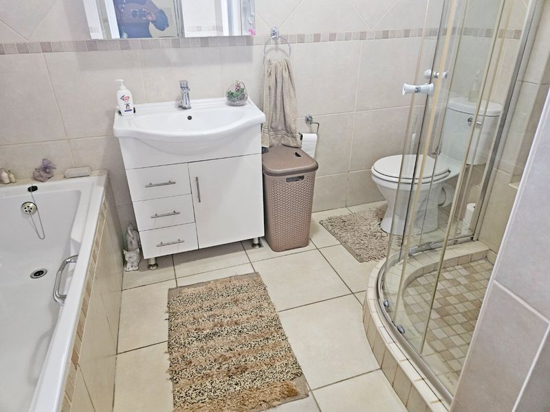 A functional bathroom featuring a vanity unit, bathtub, separate shower enclosure, and toilet with neutral wall and floor tiling.