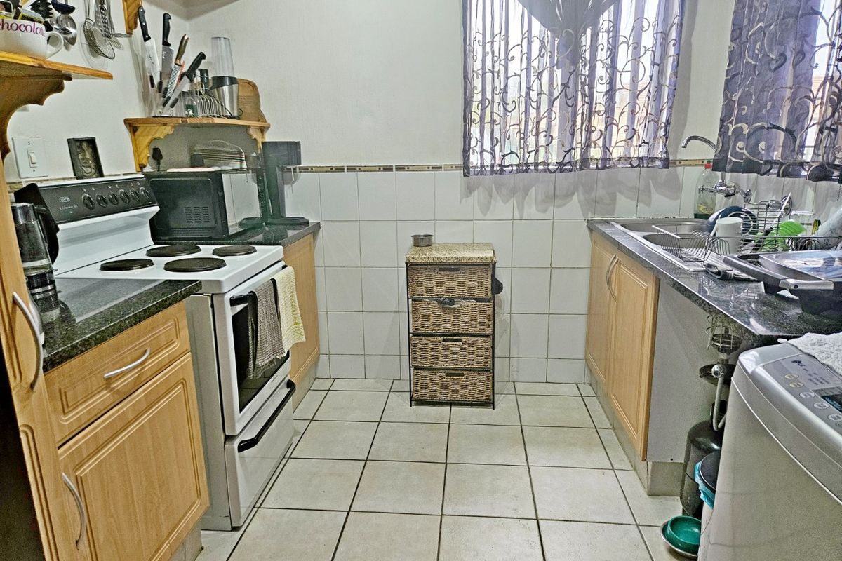 A functional kitchen featuring laminate cabinetry, granite countertops, a built-in electric stove, and a double sink with tiled backsplash and flooring.