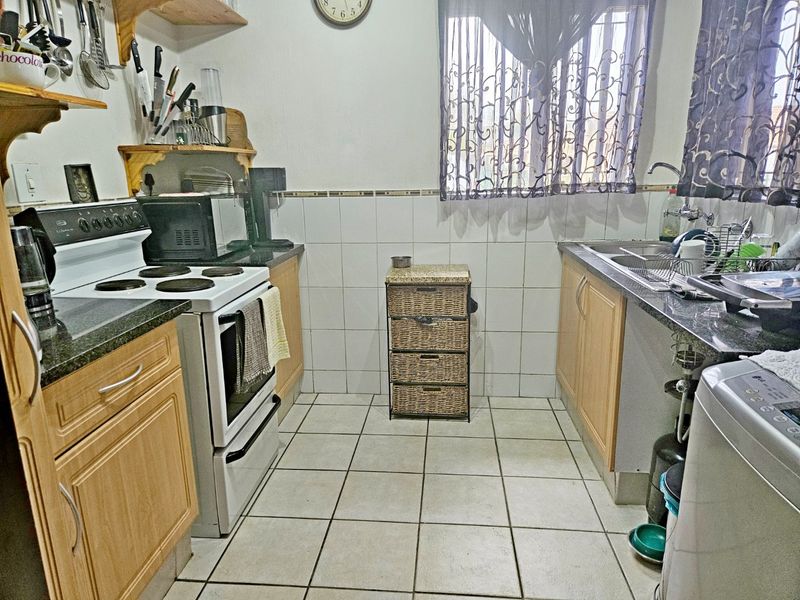 A functional kitchen featuring laminate cabinetry, granite countertops, a built-in electric stove, and a double sink with tiled backsplash and flooring.
