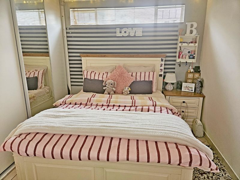 A cozy bedroom featuring a built-in mirrored wardrobe and a high-level clerestory window with fitted venetian blinds.