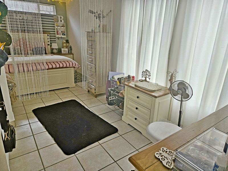 A bedroom featuring tiled flooring and horizontal window blinds, offering a functional space with neutral finishes.