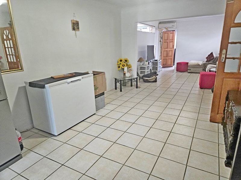 Open-plan living area featuring ceramic floor tiles, a wall-mounted air conditioning unit, and direct access to an exterior door.
