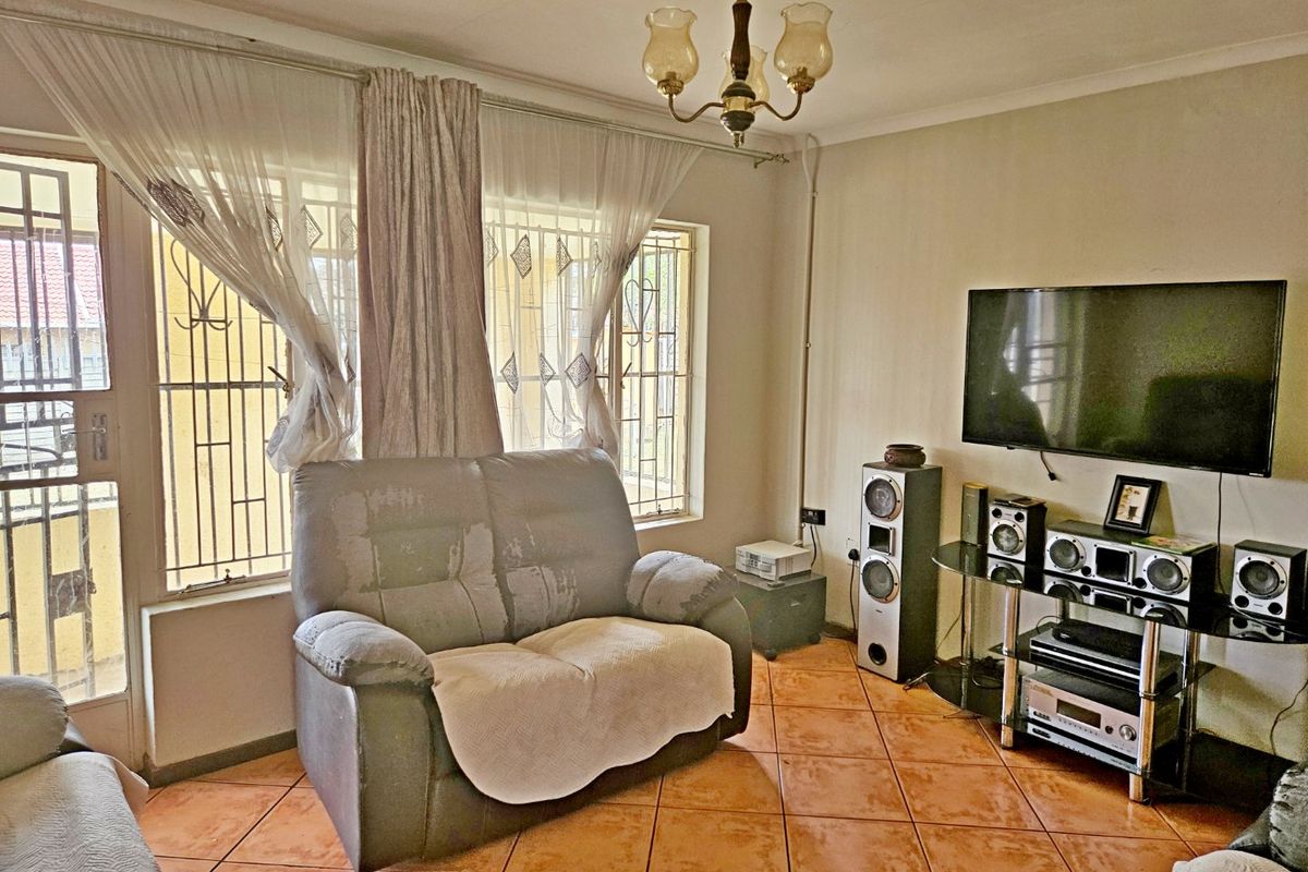 A living room featuring ceramic floor tiles, security bars on windows, and a security gate, providing a functional space with basic finishes.