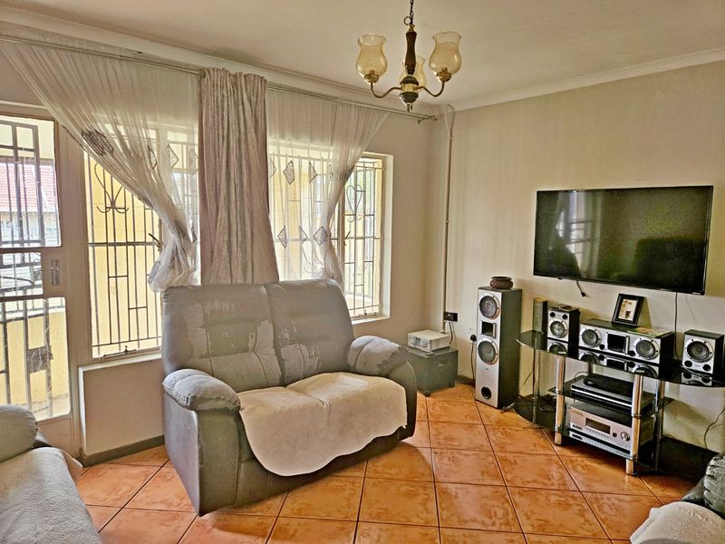 A living room featuring ceramic floor tiles, security bars on windows, and a security gate, providing a functional space with basic finishes.