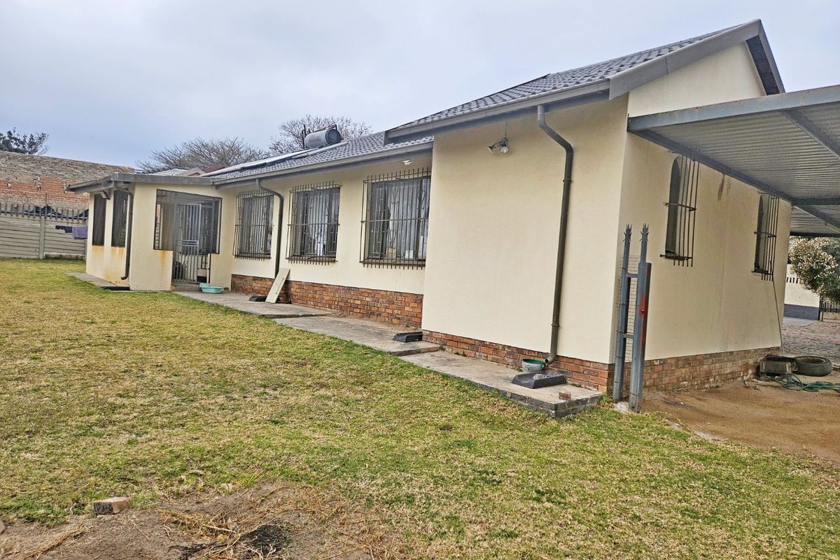 Rear view of a single-story house featuring a tiled roof, brick plinth, security bars on windows, and an attached carport with a surrounding lawn.