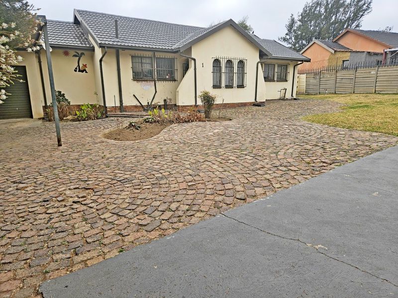 Front exterior view of a single-story house featuring a cobblestone driveway, tiled roof, and security bars on windows.