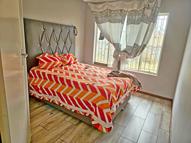 A functional bedroom featuring tiled flooring and a window fitted with security bars, providing natural light.