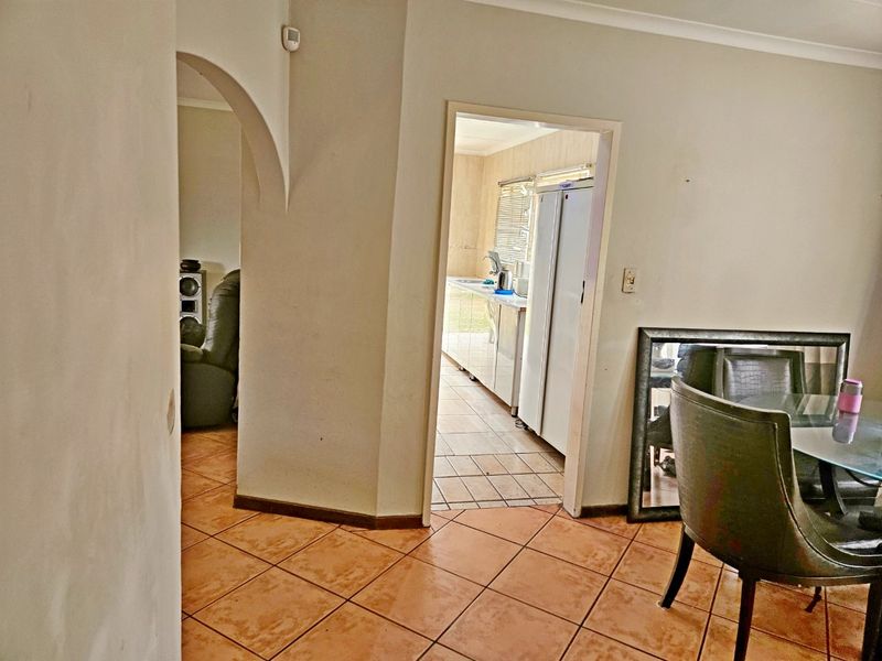 A tiled hallway featuring an arched entryway leading to the kitchen and adjacent living area, showcasing a functional layout with neutral wall finishes.