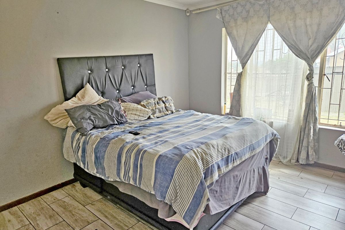 A functional bedroom featuring tiled flooring and a window fitted with security bars, offering a neutral base for potential interior updates.