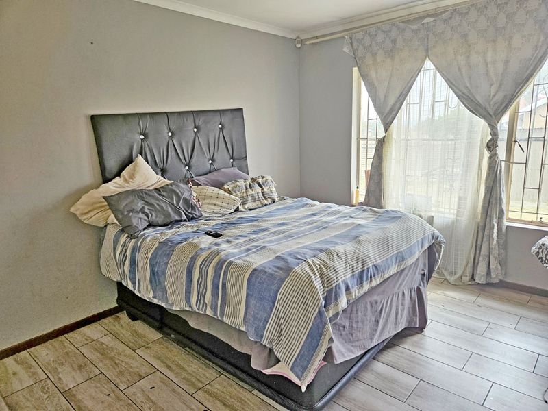A functional bedroom featuring tiled flooring and a window fitted with security bars, offering a neutral base for potential interior updates.