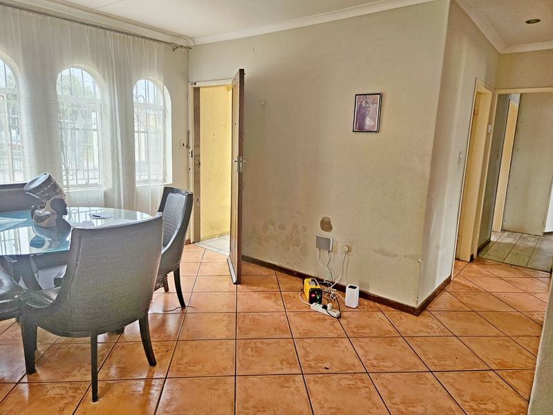Dining area featuring ceramic floor tiles, arched windows with security bars, and coved ceilings. The walls show visible signs of damp and surface damage.