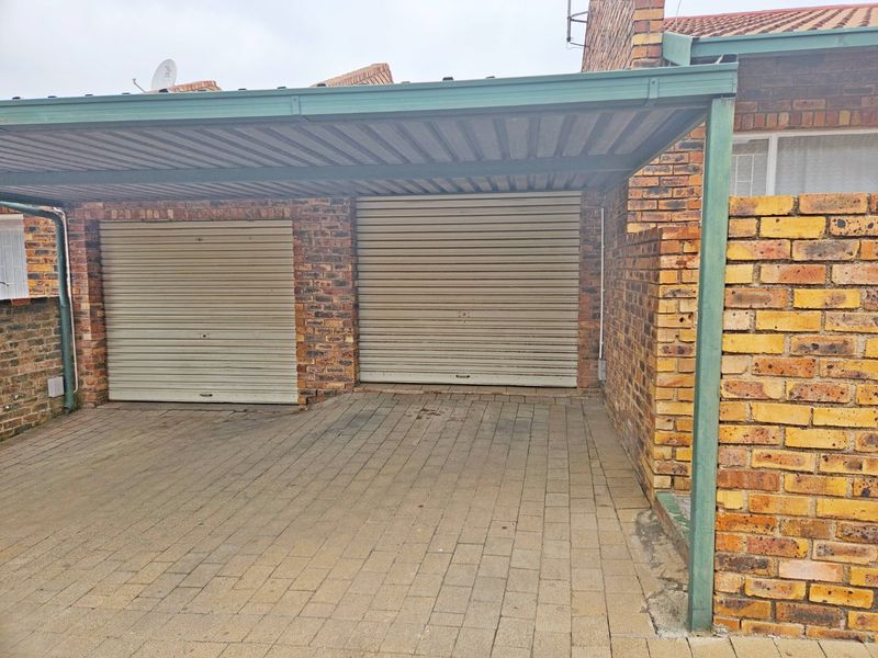 A double garage featuring roller doors and an attached carport, finished with facebrick and a paved driveway.